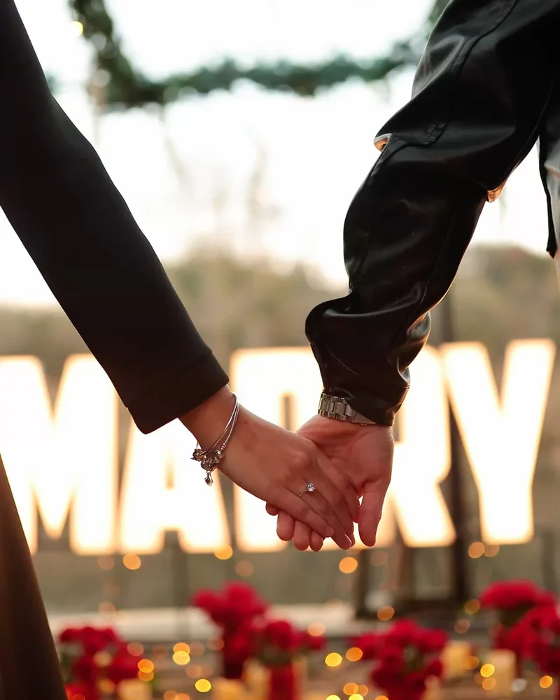 Işıklı MARRY harflerinin önünde el ele tutuşan çift